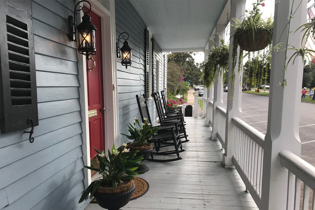 A porch with rocking chairs, potted plants, and hanging planters.