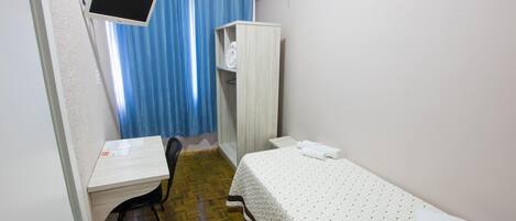 Una habitación pequeña y limpia, con escritorio, silla, cama y armario.