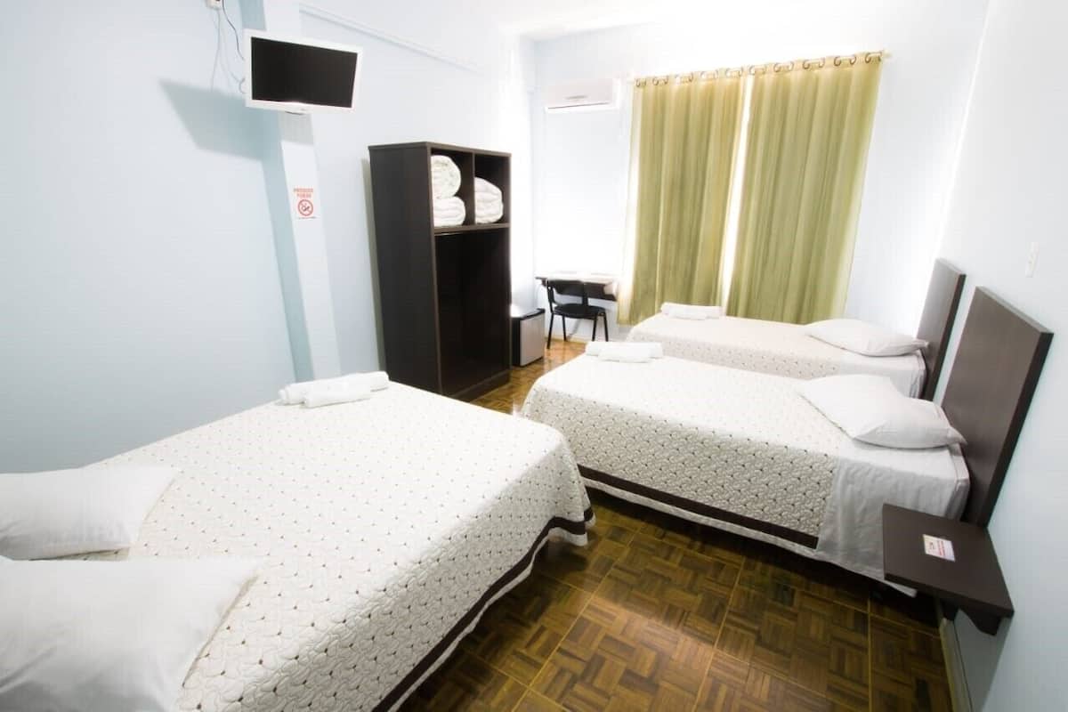 Habitación de hotel con dos camas, un escritorio, un armario y una ventana con cortinas.