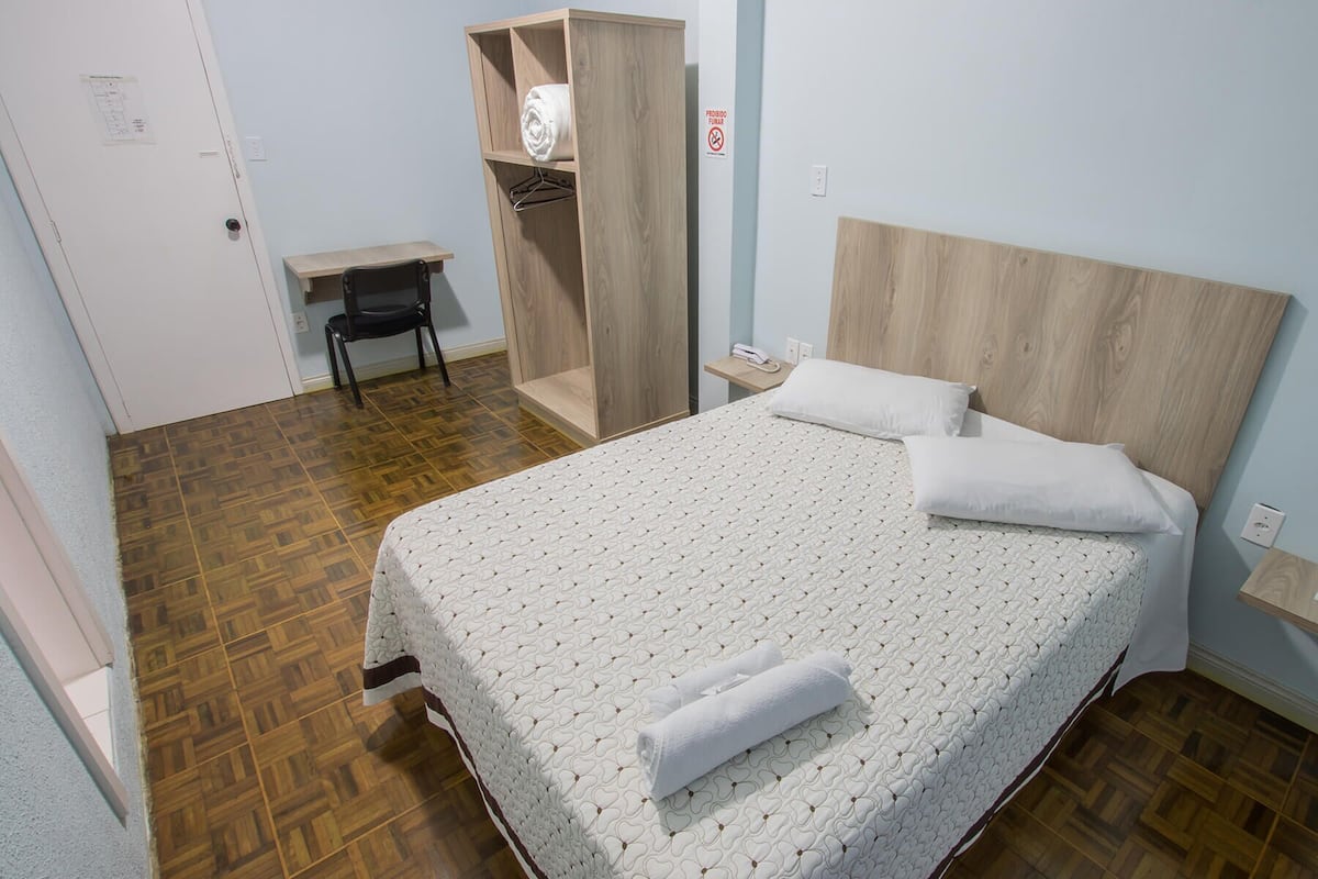 Habitación de hotel ordenada con cama, escritorio y armario.
