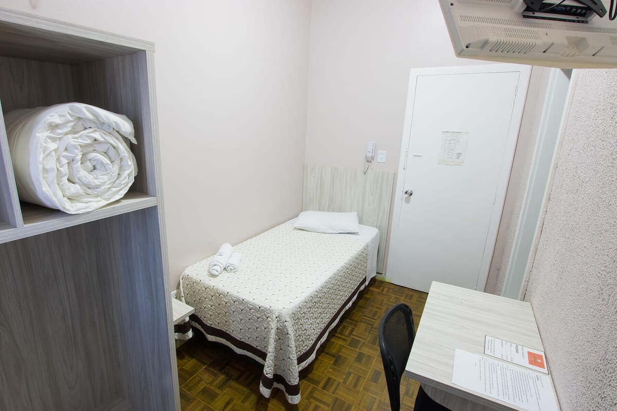 Una habitación pequeña y ordenada con una cama individual, una silla, un escritorio y un armario.