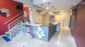 A hotel reception area with a modern design, including a reception desk, a clock, and a sign prohibiting smoking. - Hotel Conda (Chapecó)