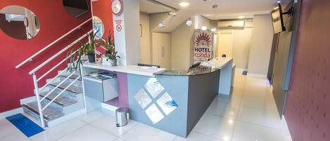 A hotel reception area with a modern design, including a reception desk, a clock, and a sign prohibiting smoking.