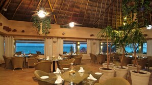 Een restaurant met gedekte tafels, grote potplanten en uitzicht op zee.
