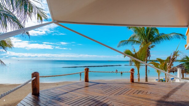 Een houten terras met een touwbescherming, palmbomen en een heldere blauwe zee.