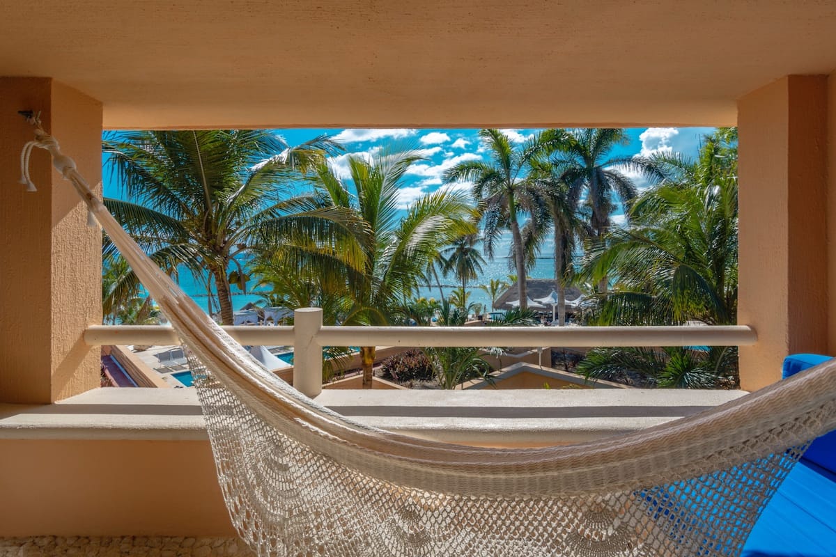 Un hamac sur un balcon avec vue sur des palmiers et une piscine.