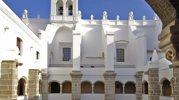 A courtyard with a central lawn, surrounded by white buildings with multiple arches and a bell tower. - Amazing House in Evora (Évora)