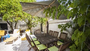 An outdoor patio with a wooden table and chairs, surrounded by greenery and a white wall. - Amazing House in Evora (Évora)