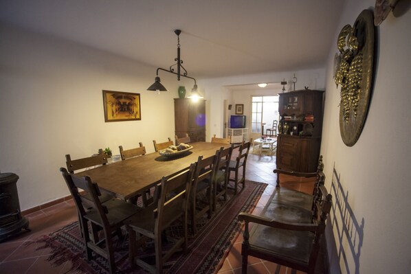A dining area with a wooden table and chairs, a chandelier, and a television in the background.