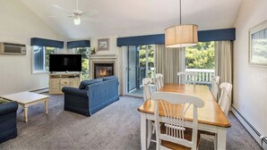 Una sala de estar con sofá, televisión, chimenea, mesa de comedor, sillas y ventilador de techo.