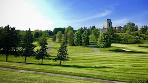 Un campo de golf con un camino despejado, árboles y un edificio al fondo.