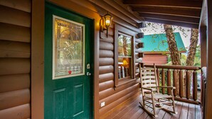 Eine Holzhütte mit einer grünen Tür, einem Schaukelstuhl auf der Veranda und einer Laterne an der Wand.