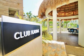 A sign for 'CLUB KAYAK' with a thatched roof structure and palm plants in the background. - Mayakoba by Select (Playa del Carmen)