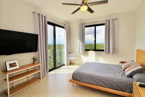 A bedroom with a bed, a TV, a ceiling fan, and a balcony with a view of greenery. - Mayakoba by Select (Playa del Carmen)