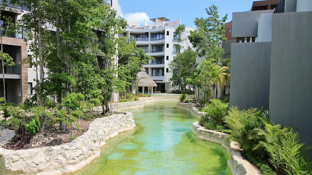Ein modernes Hotel mit einem zentralen Wasserspiel, umgeben von üppigem Grün und Steinwegen.