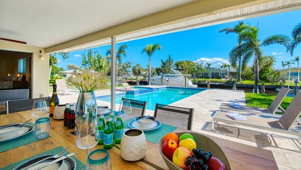 A dining area with a view of a pool, outdoor seating, and tropical landscaping.
