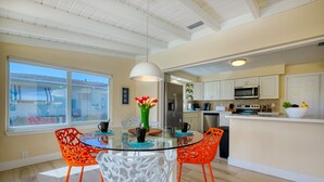 A modern kitchen with white cabinets, a microwave, and a refrigerator. There is a dining area with a glass table and orange chairs.