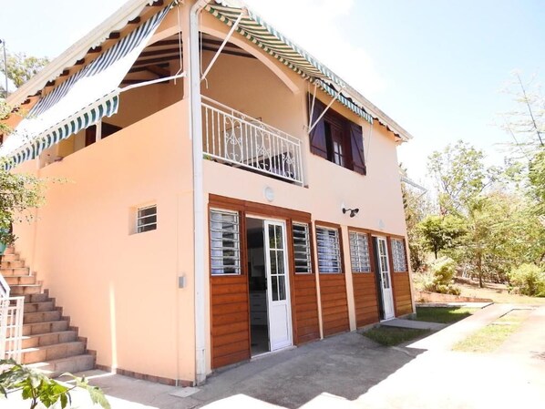 A two-story building with a balcony, a staircase, and a small garden area. - Gîte MORINGA (Bouillante)