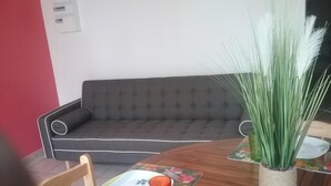 A dining area with a round wooden table, a grey sofa, and a potted plant. - Gîte MORINGA (Bouillante)