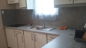 A kitchen with white cabinets, a stainless steel sink, and a window with sheer curtains. - Gîte MORINGA (Bouillante)