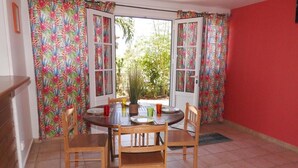A dining area with a round table, four wooden chairs, and a potted plant. - Gîte MORINGA (Bouillante)