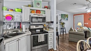 Una cocina moderna con armarios blancos, microondas integrado y estufa. Hay un comedor con sofá y sillas.