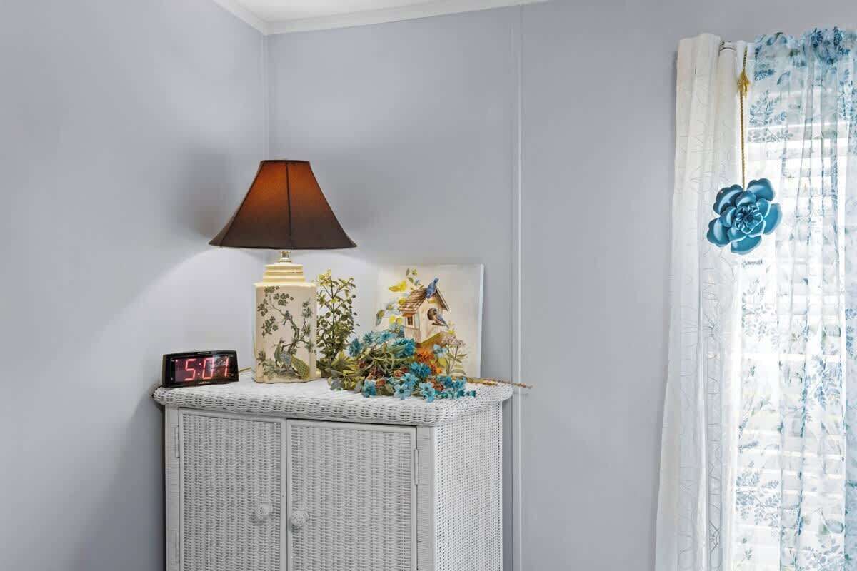 Une pièce avec une armoire en osier, une lampe, une horloge et un rideau à motifs floraux.