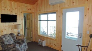 A wooden-paneled room with a television, a chair, a lamp, and a door leading outside. - Cottage #22 - 3 bedroom/1 bath (Cape Vincent)