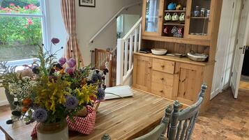A dining area with a wooden table, chairs, a vase of flowers, a cabinet with kitchenware, and a staircase.