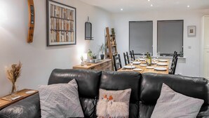 Een moderne woonkamer met een zwarte leren bank, een houten eettafel voor vier personen en een boekenkast met boeken en decoratieve objecten.