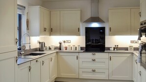 Een moderne keuken met witte kasten, een roestvrijstalen afzuigkap en verlichting onder de kasten.