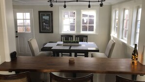 A dining room with a wooden table and chairs, a chandelier, and large windows.
