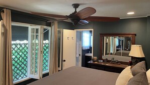 A bedroom with a bed, a ceiling fan, a dresser, a mirror, and a view of a green outdoor area through a sliding door.