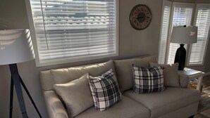 En beige sofa med to ternede puder, en gulvlampe og et vægur.
