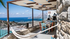 Eine Terrasse mit einer Hängematte, Sitzgelegenheiten im Freien und Blick auf das Meer und die Berge.