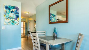 Un comedor con una mesa y sillas de color claro, un florero y dos cuadros en la pared.
