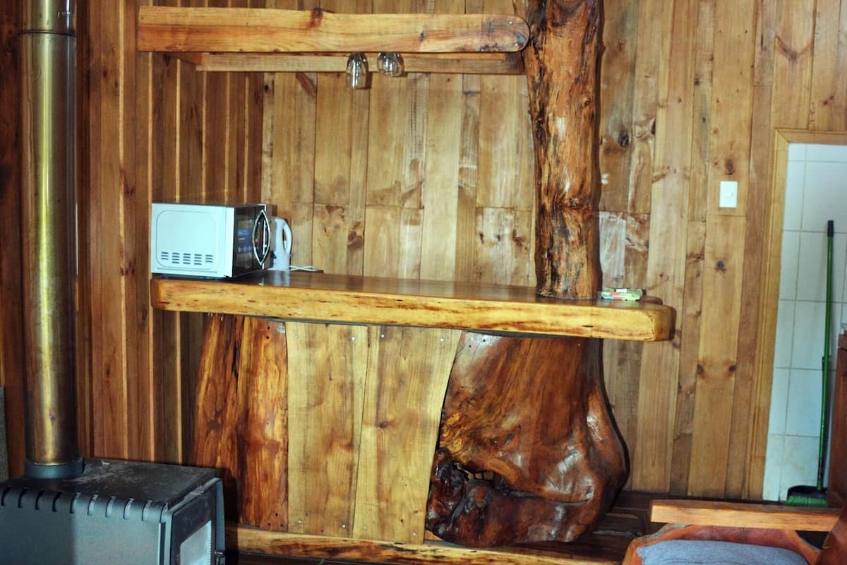 A wooden interior with a wooden wall, a wooden table, a sofa, a rug, and a stove.