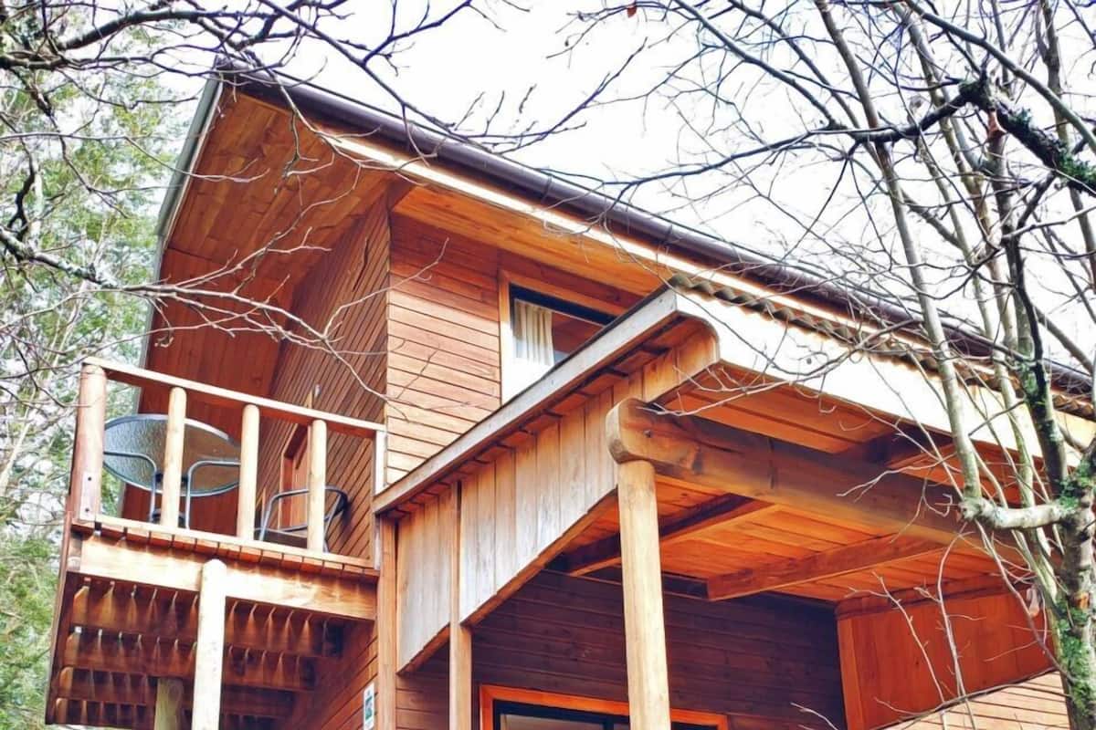 A wooden cabin with a balcony, a staircase, and a dining area.