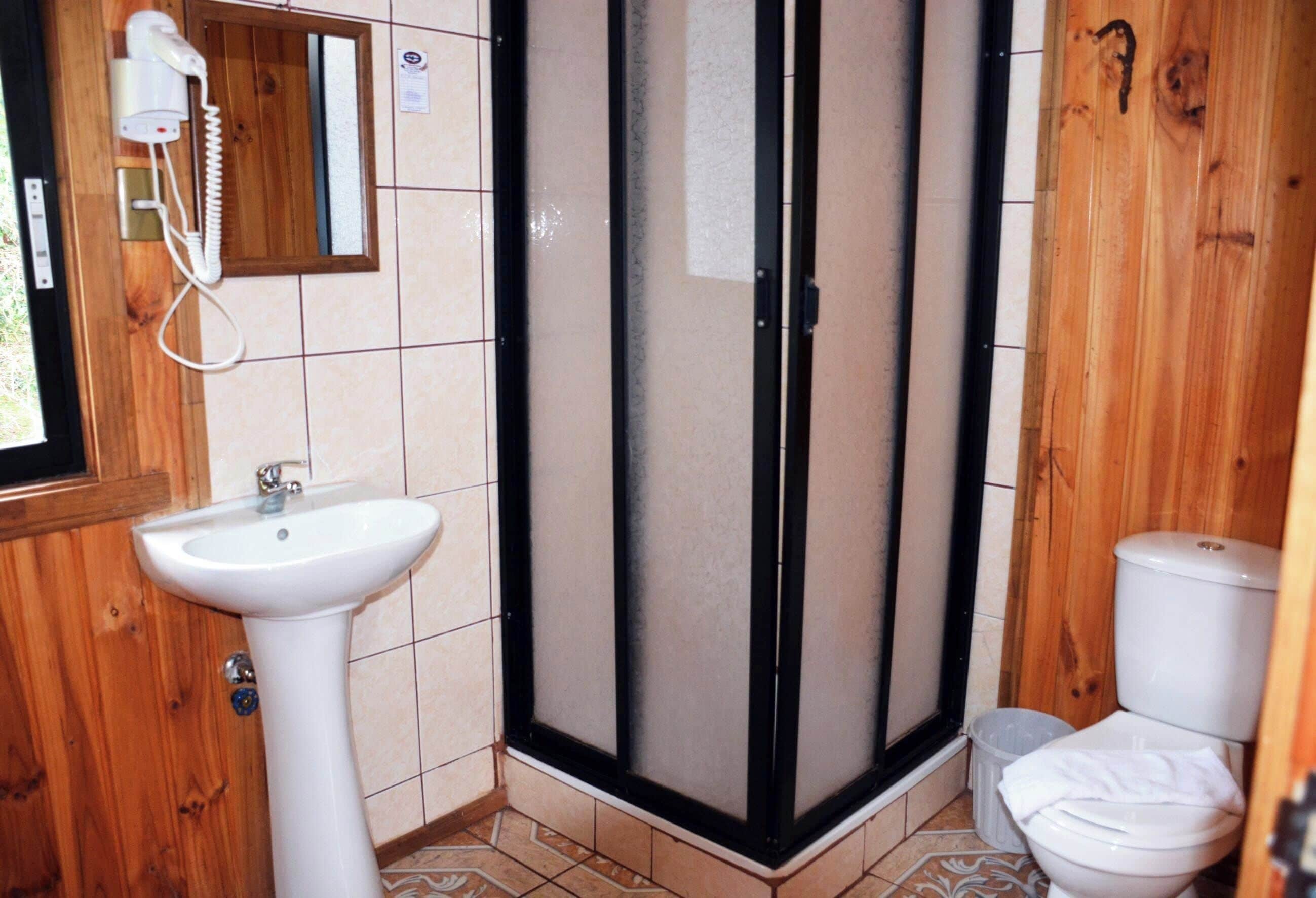 A bathroom with a wooden interior, a white sink, a glass shower enclosure, and a toilet.