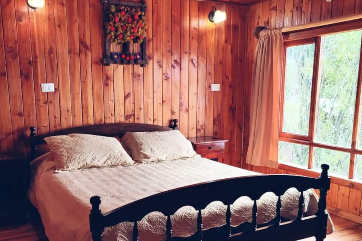 A wooden-paneled bedroom with a bed, nightstands, and a window with curtains.