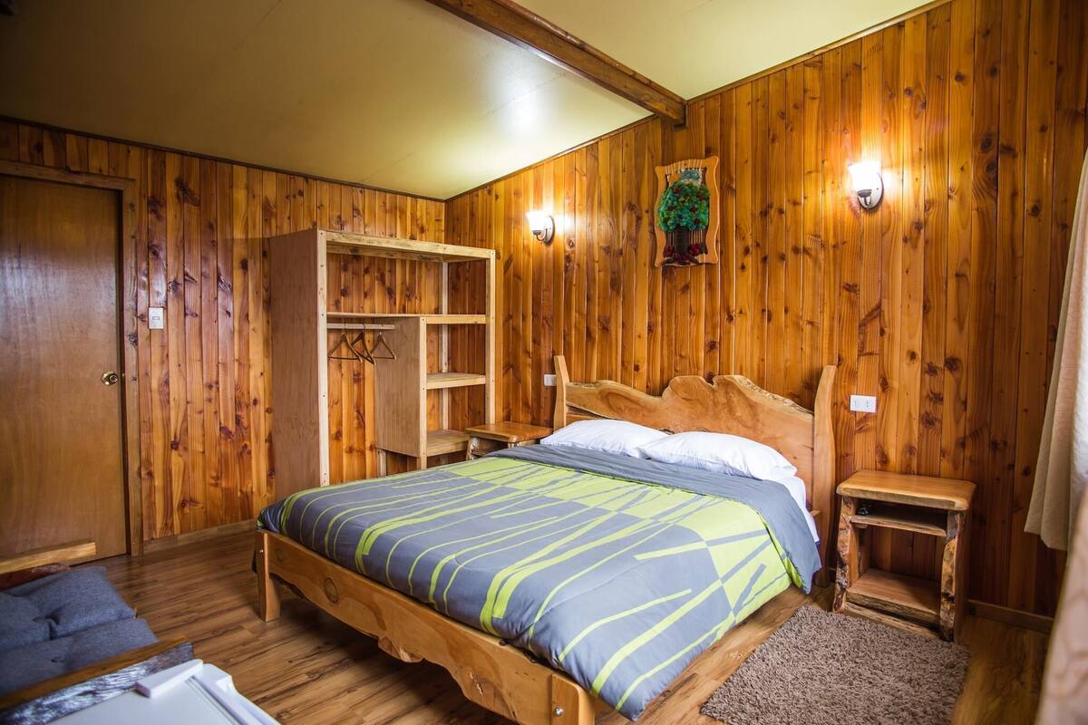 A wooden-paneled room with a bed, a wardrobe, and a small table.