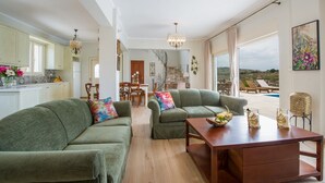 A spacious living room with a green sofa set, a wooden coffee table, and a dining area in the background. - 100mt to the Beach ★ Stunning Sunset ★ Private pool ★ Exclusive location (Kokkino Chorio)