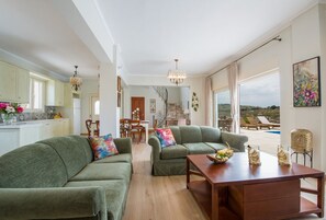 Een ruime woonkamer met een groene zithoek, een houten salontafel en een eethoek op de achtergrond.
