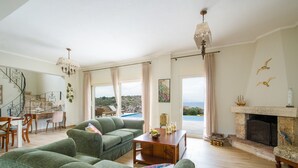 A spacious living room with a green sofa, a wooden dining table, and a fireplace. - 100mt to the Beach ★ Stunning Sunset ★ Private pool ★ Exclusive location (Kokkino Chorio)