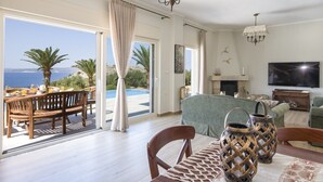 A spacious living room with a large TV, a fireplace, and a view of the sea. - 100mt to the Beach ★ Stunning Sunset ★ Private pool ★ Exclusive location (Kokkino Chorio)