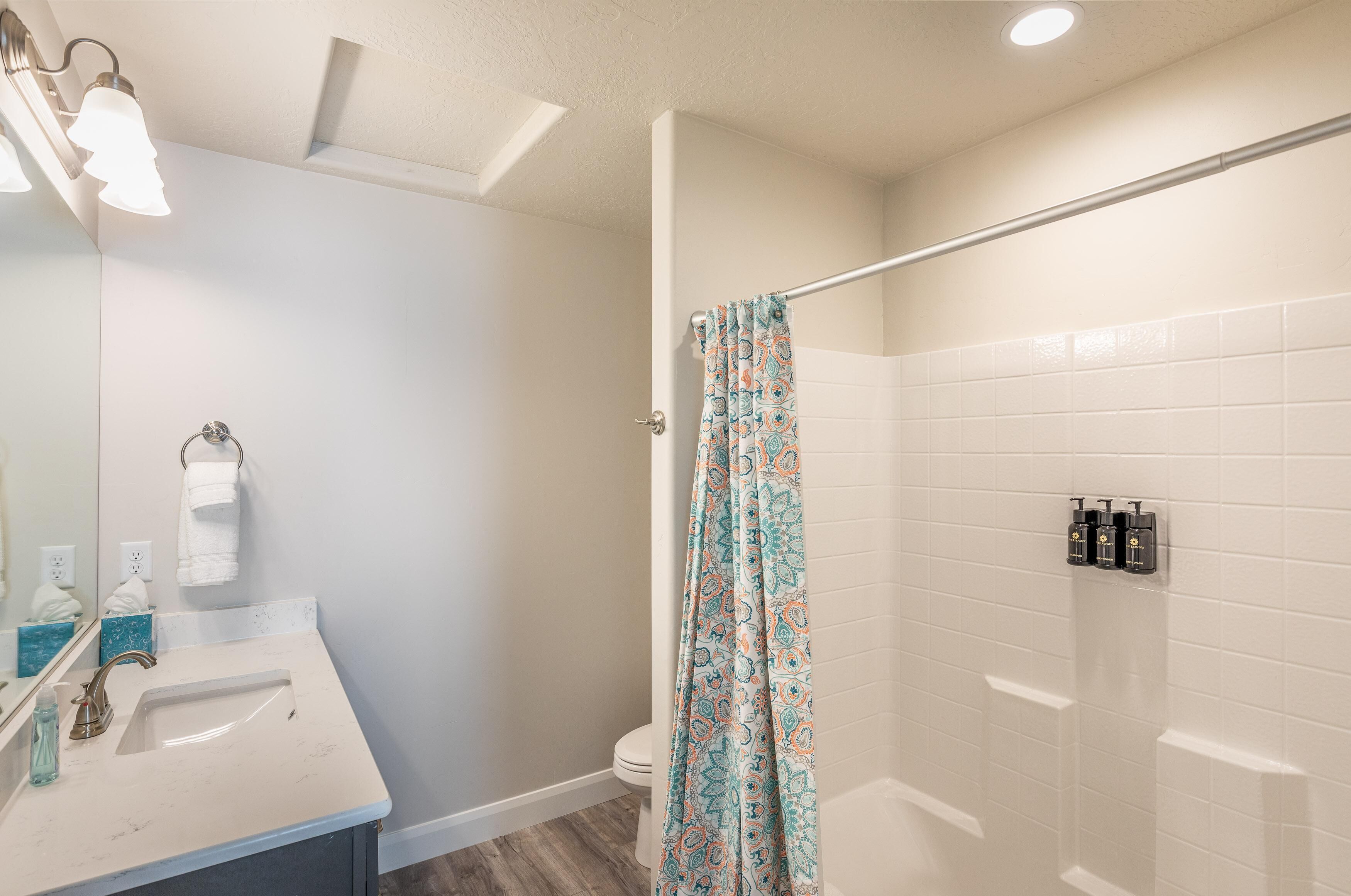 Une salle de bain équipée d’un lavabo, d’un miroir, d’un porte-serviettes, d’un rideau de douche et de toilettes.