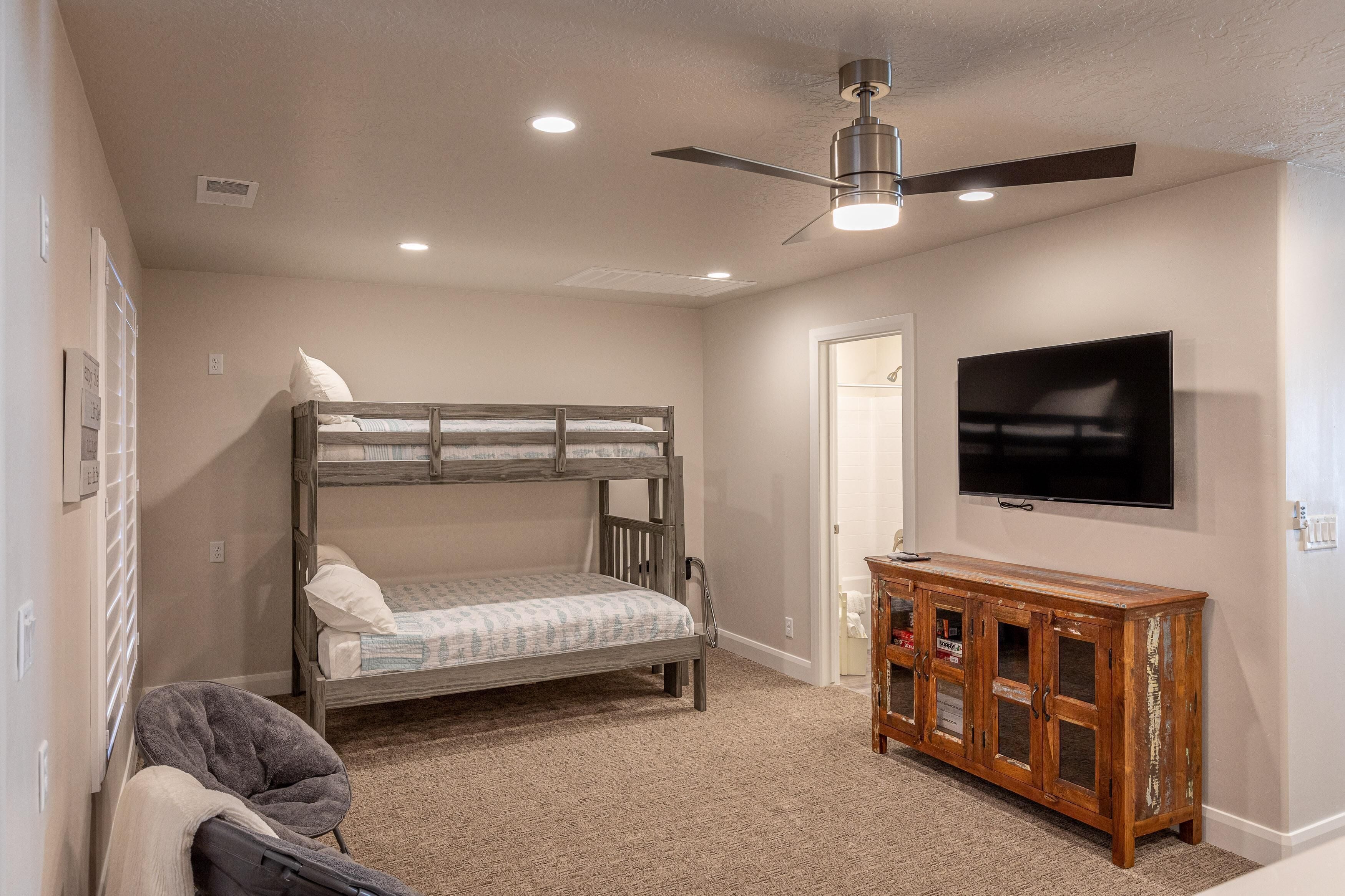 A bedroom with a bunk bed, a wooden cabinet, a television, and a ceiling fan.