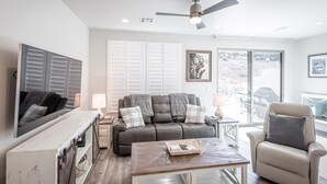 Un salon comprenant un canapé, une table basse et un fauteuil, un ventilateur de plafond et de grandes fenêtres.