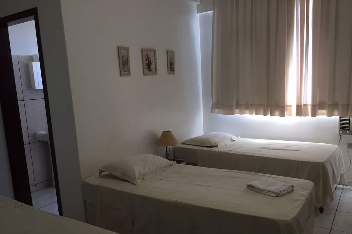 Hotellihuone, jossa on kaksi erillistä sänkyä, pieni pöytä lampun kanssa ja ikkuna, jossa on verhot.