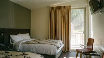 A hotel room with two beds, a chair, a TV, and a window with curtains.